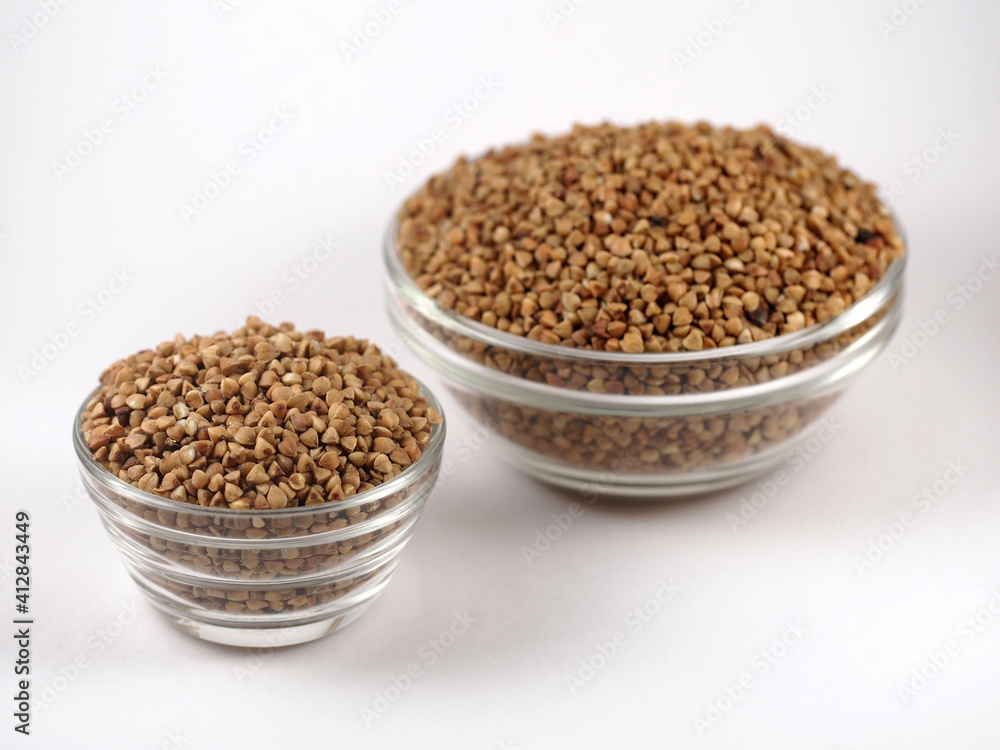Two bowls with raw uncooked buckwheat on white background. Top view. The texture of dry buckwheat. Two bowls with raw uncooked buckwheat on white background. Top view. The texture of dry buckwheat.