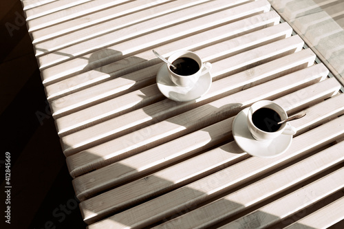 Two cups of black coffee, on a light wood table. View from above.