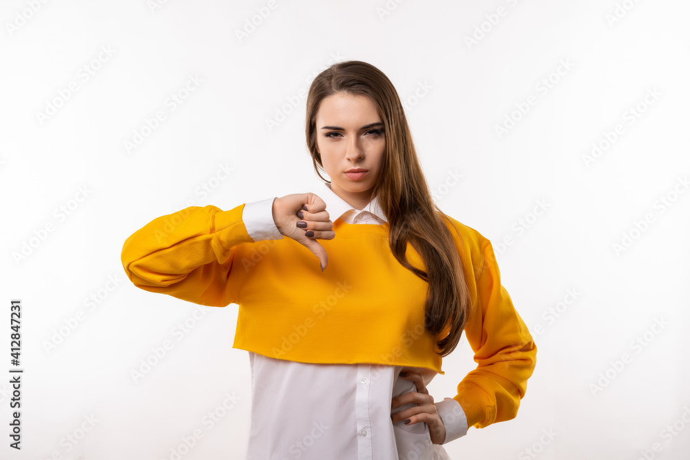 Portrait of attractive brunette girl showing thumb down. Human emotions, gesture concept. Studio shot, white background Portrait of attractive brunette girl showing thumb down. Human emotions, gesture concept. Studio shot, white background