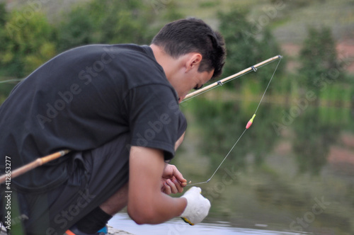 Young man putting worm on fishing rod or pole at water background