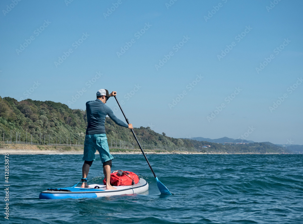 Naklejka premium Active man paddling on stand up paddle board on sea water at coast background