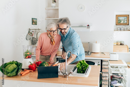 Senior couple preparing healthy smoothie in kitchen and using tablet to read recipe