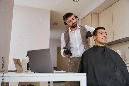 Hair dresser making hair cut with special instrument for pleased customer in apartments
