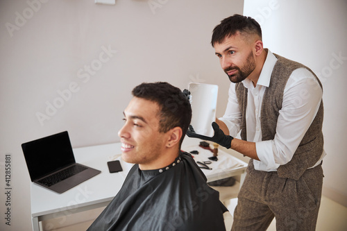 Professional barber showing reflection in the mirror of pleased customer in beauty salon