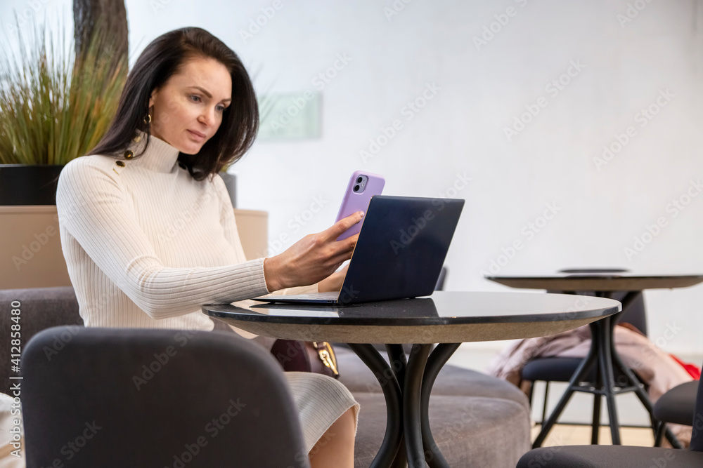 beautiful business woman typing on the phone while sitting at the table with laptop beautiful business woman typing on the phone while sitting at the table with laptop