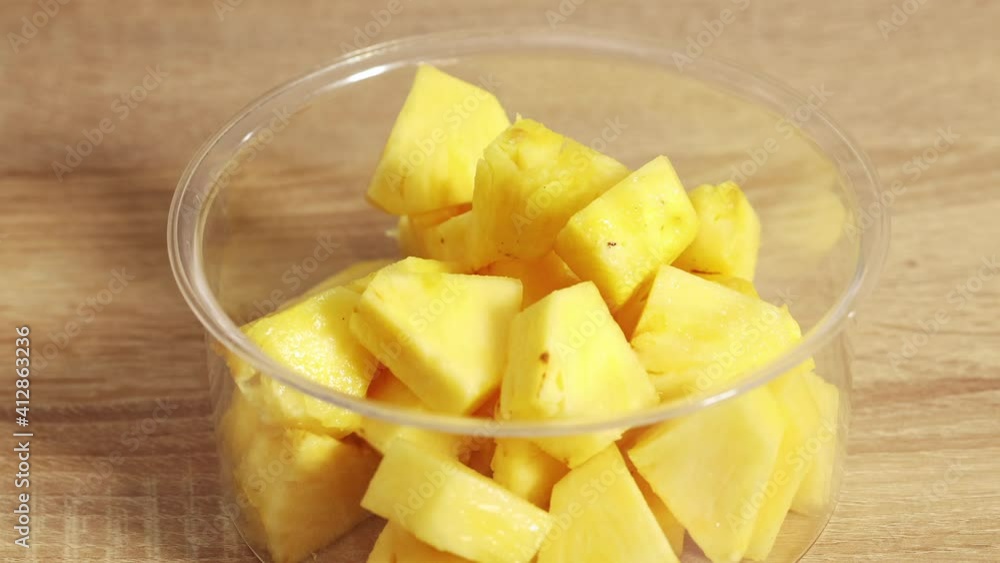 female hands put in bowl fresh ripe pineapple fruit pieces and at domestic kitchen for making healthy breakfast smoothie. home cooking close up female hands put in bowl fresh ripe pineapple fruit pieces and at domestic kitchen for making healthy breakfast smoothie. home cooking close up