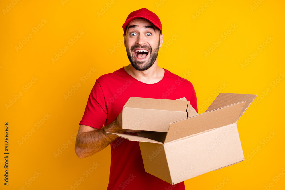 Photo of impressed delivery man wear red outfit holding brown boxes isolated yellow color background Photo of impressed delivery man wear red outfit holding brown boxes isolated yellow color background