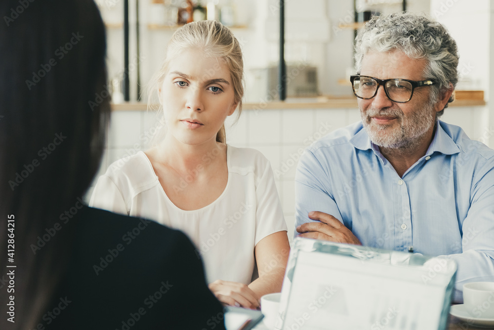 Fototapeta premium Young and mature customers meeting with financial expert. Back of businesswoman using laptop with graphs on display and talking to clients. Business meeting concept