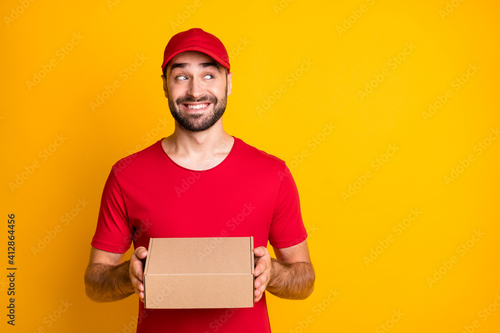Photo portrait of curious courier holding carton box for delivery looking blank space isolated on vibrant yellow color background Photo portrait of curious courier holding carton box for delivery looking blank space isolated on vibrant yellow color background