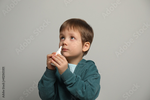 Little boy using nasal spray on light grey background