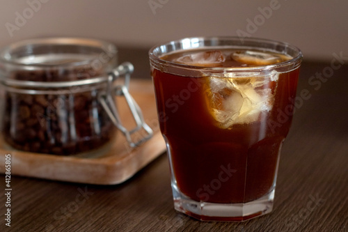 Cold brew Ice coffee with ice cubes and jar with coffee beans on wooden plate.