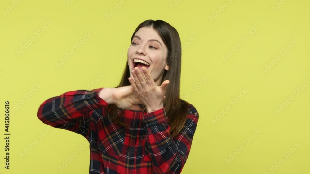 Happy mercantile brunette woman in checkered shirt showing pay me gesture, looking at camera with cunning expression, asking payment. Indoor studio shot isolated on yellow background Happy mercantile brunette woman in checkered shirt showing pay me gesture, looking at camera with cunning expression, asking payment. Indoor studio shot isolated on yellow background