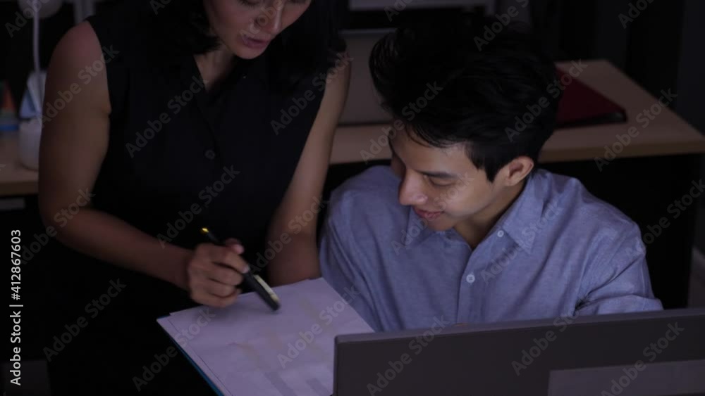 Front view, high angle shot of female boss teaching, coaching male employee, discussing business while power off, talking, and smiling, at the dark workplace. Asian and overtime business concept. Front view, high angle shot of female boss teaching, coaching male employee, discussing business while power off, talking, and smiling, at the dark workplace. Asian and overtime business concept.