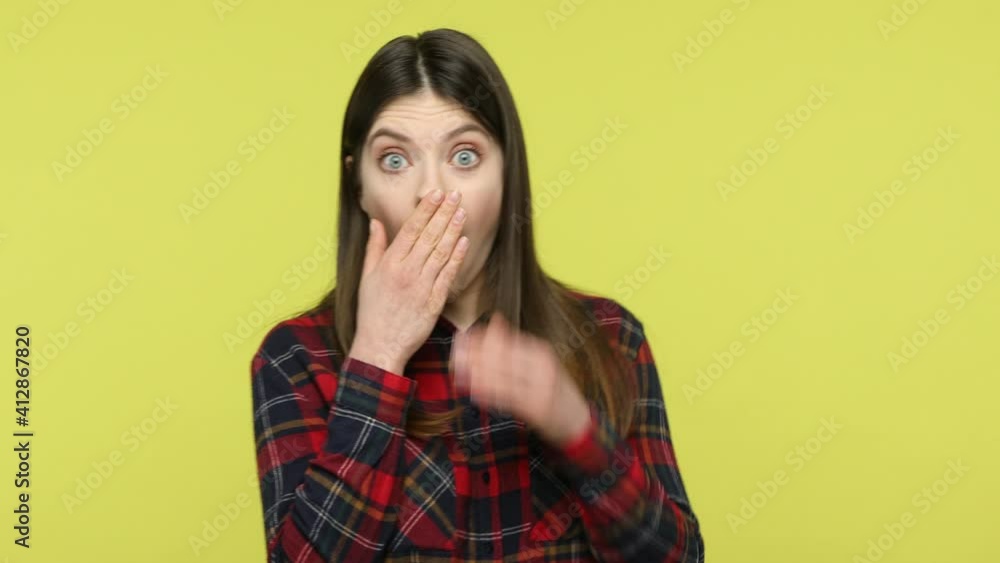 Shocked bewildered woman in checkered shirt closing mouth and throwing out key, keeping secrets, knowing private important information. Indoor studio shot isolated on yellow background Shocked bewildered woman in checkered shirt closing mouth and throwing out key, keeping secrets, knowing private important information. Indoor studio shot isolated on yellow background