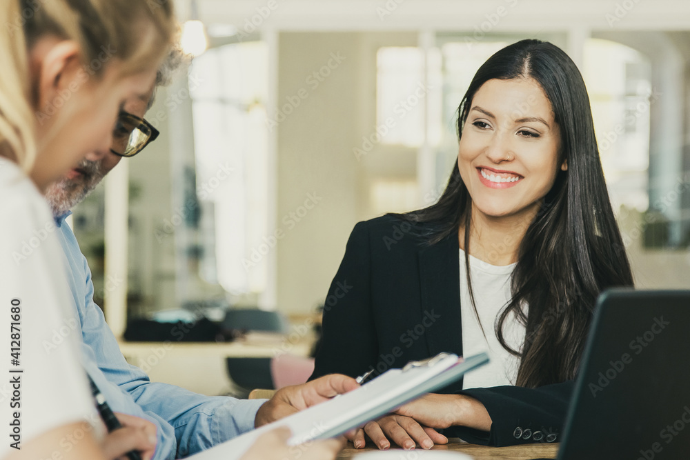 Couple of customers meeting with agent and reading insurance agreement. Young woman in formal jacket smiling and looking at clients. Business meeting concept Couple of customers meeting with agent and reading insurance agreement. Young woman in formal jacket smiling and looking at clients. Business meeting concept