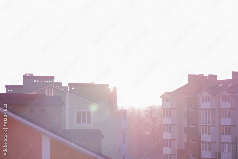 Selective focus roofs of houses on a background of sunrise. Bright rays of the sun between low-rise buildings Selective focus roofs of houses on a background of sunrise. Bright rays of the sun between low-rise buildings