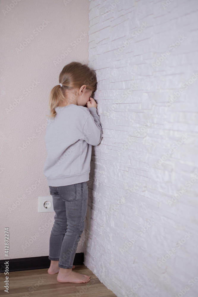 Child little girl standing in the corner of the room. Parental errors in raising children, improper punishment of children concept Child little girl standing in the corner of the room. Parental errors in raising children, improper punishment of children concept