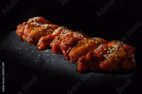 chicken wings in a sweet sauce sprinkled with sesame seeds on a black background, pepper lies on top
