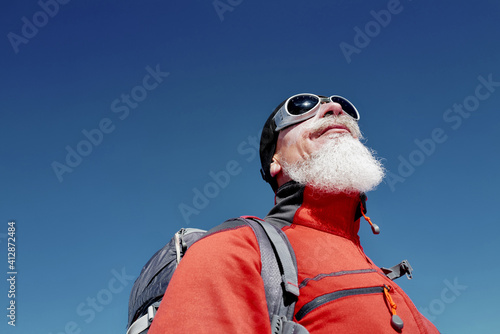 Portrait of old climber in red jacket against blue sky