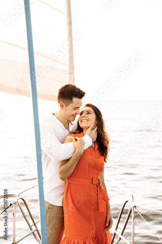 A couple in love on the edge of the yacht hug and hold hands, show love, strong hugs, blue sea, white sailing yacht. Happy valentines day