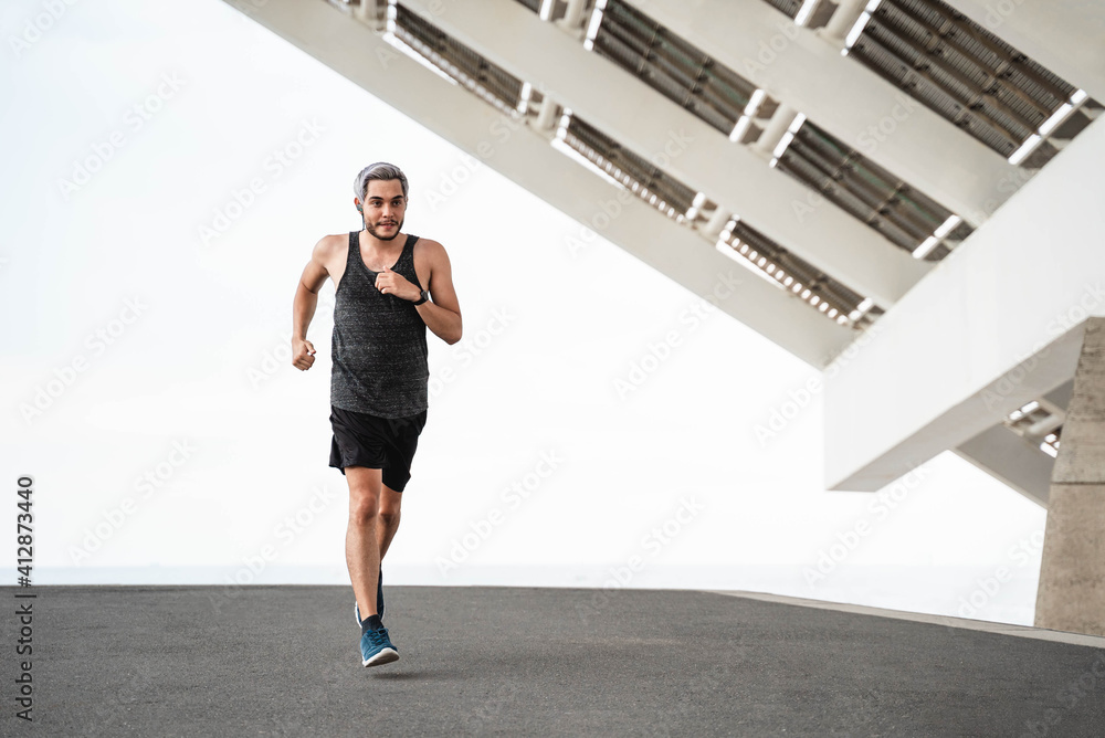 Obraz premium Young runner man doing workout routine at morning time while running outdoors in the city - Focus on face