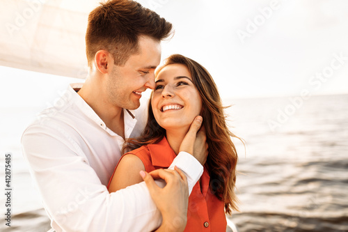 A couple in love on the edge of the yacht hug and hold hands, show love, strong hugs, blue sea, white sailing yacht. Happy valentines day