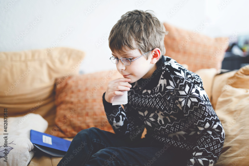 Tired little kid boy with glasses at home making homework at the morning before the school starts. Little child learning multiplication tables basics indoors. Home schooling during corona virus time