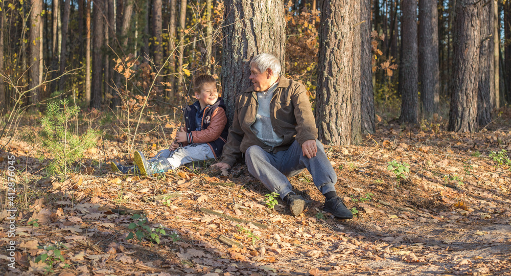 Happy child with Grandfather playing at the forest. Grandpa retiree. Retirement parent. Portrait of pensive senior man  and his grandson. Senior man having fun with his grandchild outdoor.