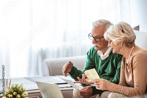 Serious senior husband and wife doing their home financials in the living room. Senior couple taking care of bills. Senior couple going over their household finances on a laptop