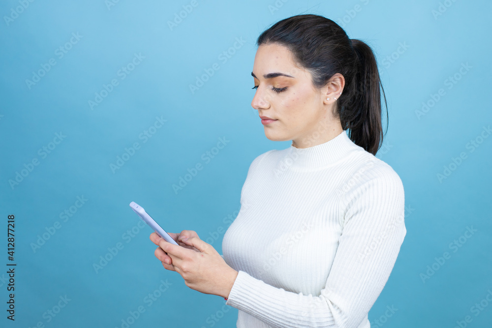 Young caucasian woman wearing white sweater over blue background texting with her phone Young caucasian woman wearing white sweater over blue background texting with her phone
