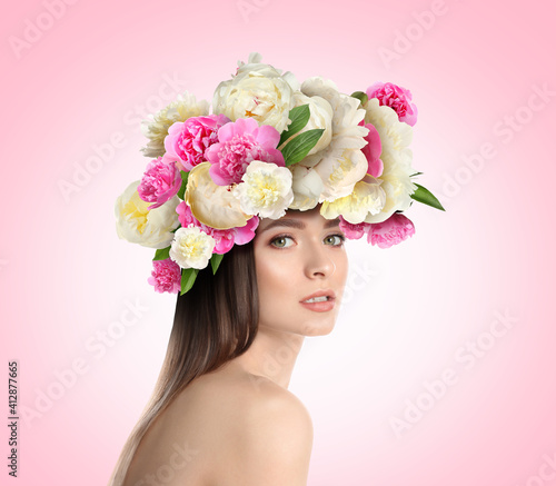 Pretty woman wearing beautiful wreath made of flowers on light pink background