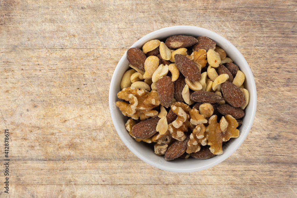 Top view of assorted nuts in a white bowl atop an old wood cutting board. Top view of assorted nuts in a white bowl atop an old wood cutting board.