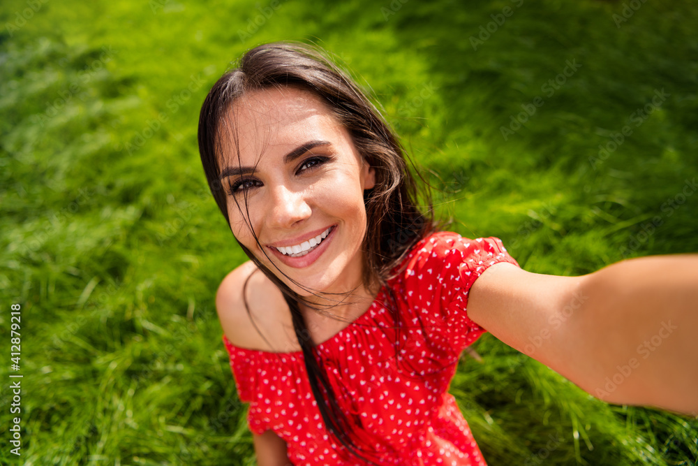 Photo of adorable young woman dressed red off-shoulders dress sitting grass making selfie outdoors backyard Photo of adorable young woman dressed red off-shoulders dress sitting grass making selfie outdoors backyard