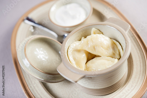 portion of ukrainian russian polish dumplings stuffed with potato in a ceramic pot served with sour cream