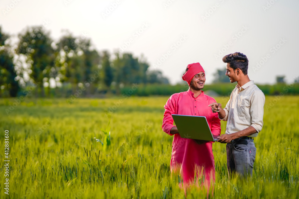 Young Indian agronomist or banker showing some information to farmer in laptop at wheat field Young Indian agronomist or banker showing some information to farmer in laptop at wheat field