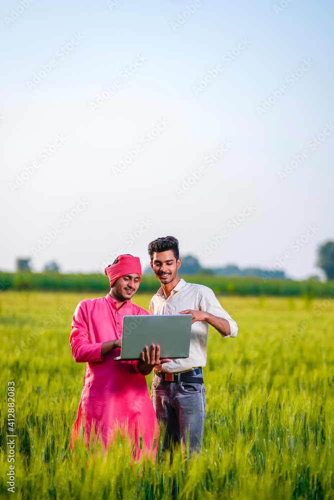 Young Indian agronomist or banker showing some information to farmer in laptop at wheat field Young Indian agronomist or banker showing some information to farmer in laptop at wheat field