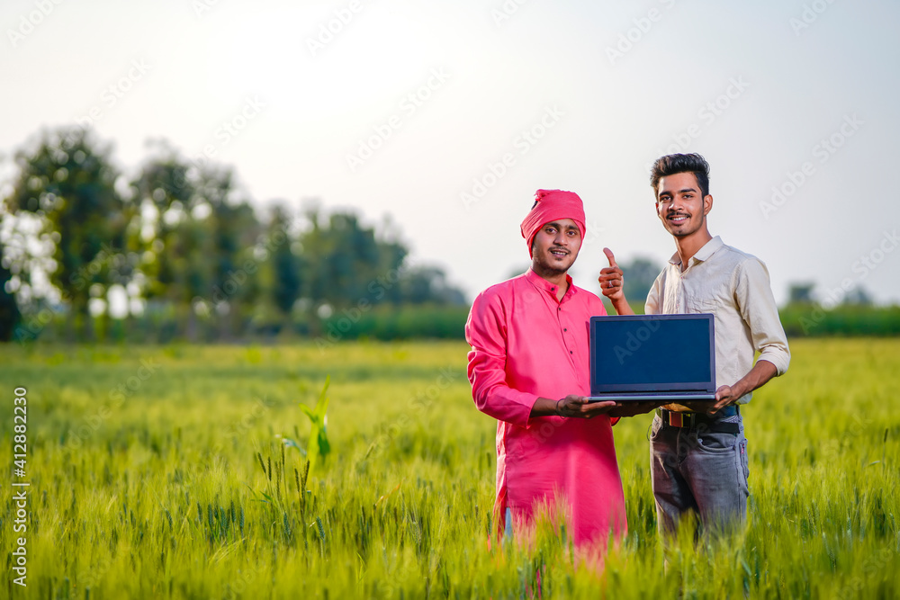 Young indian agronomist or banker showing laptop screen at green wheat field Young indian agronomist or banker showing laptop screen at green wheat field