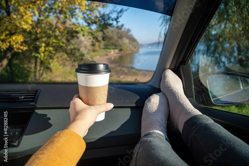 Female hand holding a cup of coffee in a car, nature