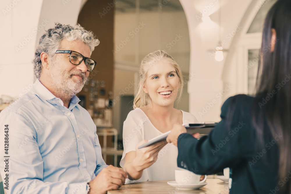 Obraz premium Happy young and mature customers meeting with agent and giving signed insurance agreement to her. Business meeting or paperwork concept