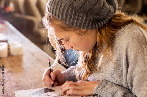 Teenage girl in a woolly hat drawing with a pencil on a sketchpad.