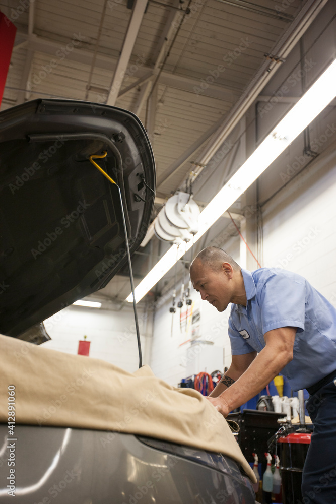 Pacific Islander mechanic works on the engine compartment in an auto repair shop Pacific Islander mechanic works on the engine compartment in an auto repair shop