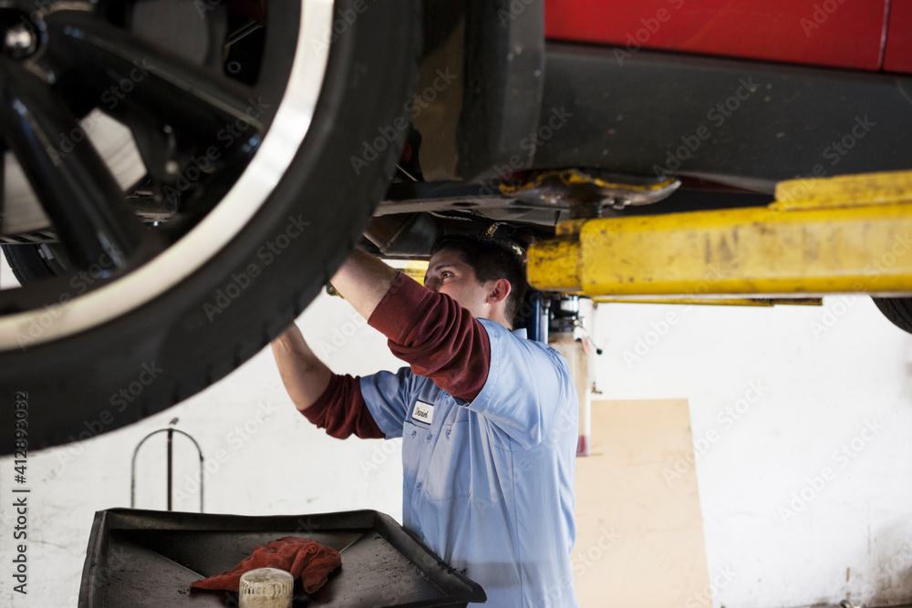 Mechanic in a repair shop works on the underside of a car up on a lift Mechanic in a repair shop works on the underside of a car up on a lift