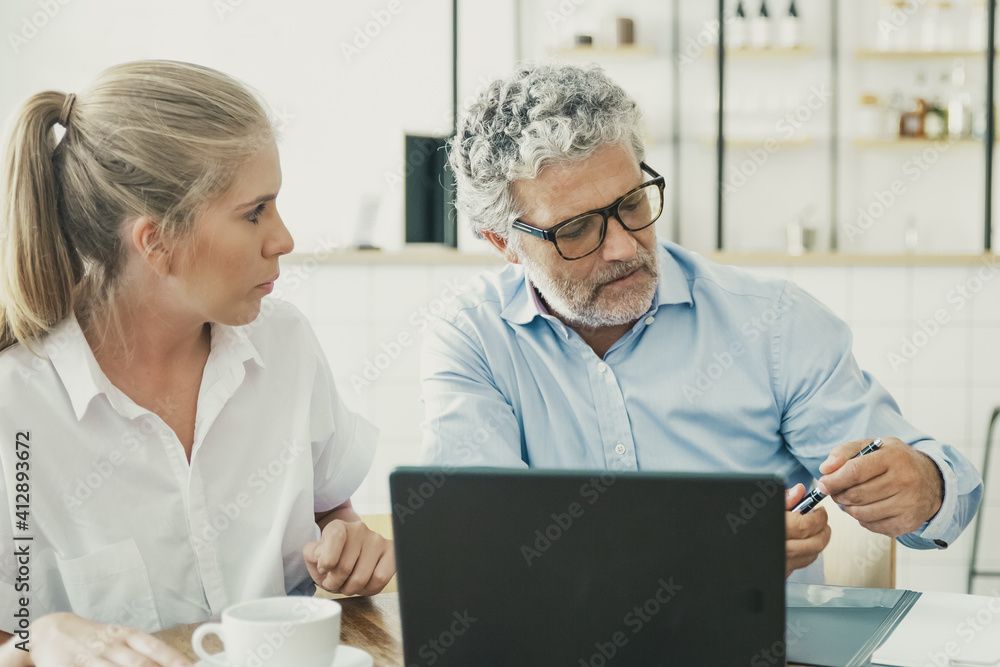 Obraz premium Businessman meeting with female agent at co-working, sitting at open laptop, taking pen for signing agreement. Medium shot. Consulting or cooperation concept