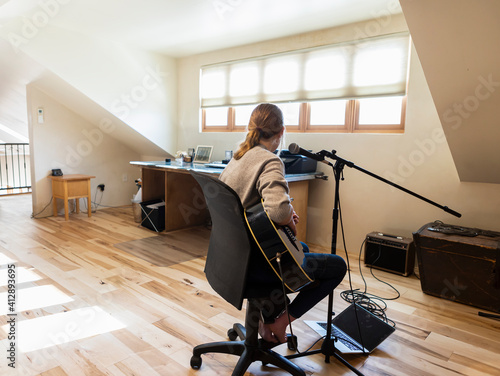 Fourteen year old teenage girl playing her guitar and singing at home in loft space photo