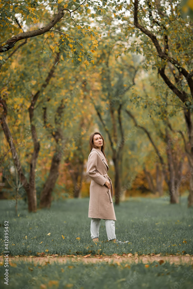 A girl with a Euro-Asian appearance in a pink coat and blue jeans with holes walks in an autumn park A girl with a Euro-Asian appearance in a pink coat and blue jeans with holes walks in an autumn park