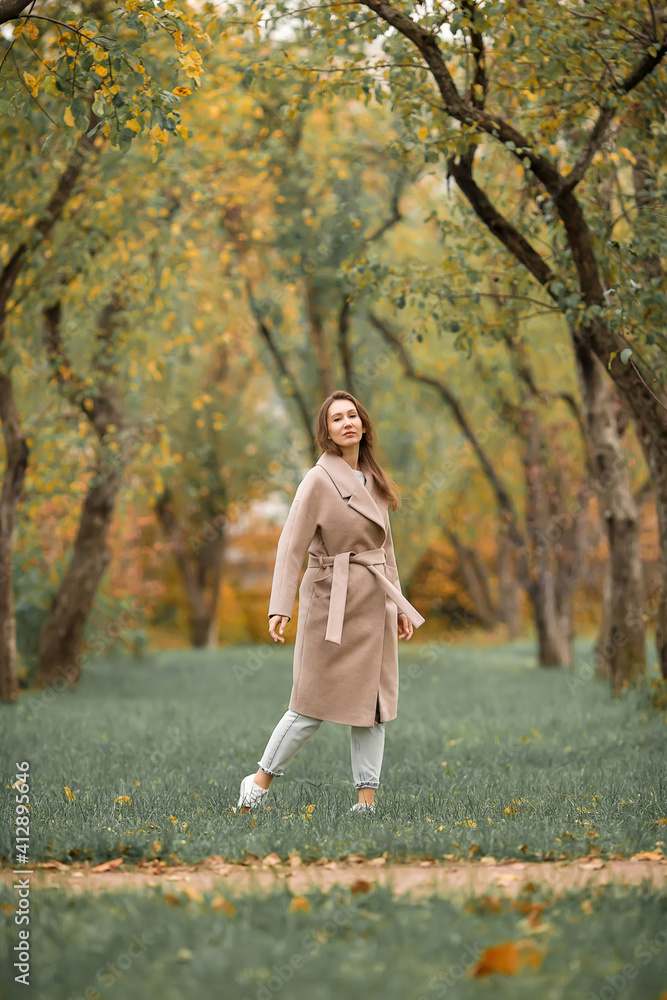 A girl with a Euro-Asian appearance in a pink coat and blue jeans with holes walks in an autumn park A girl with a Euro-Asian appearance in a pink coat and blue jeans with holes walks in an autumn park