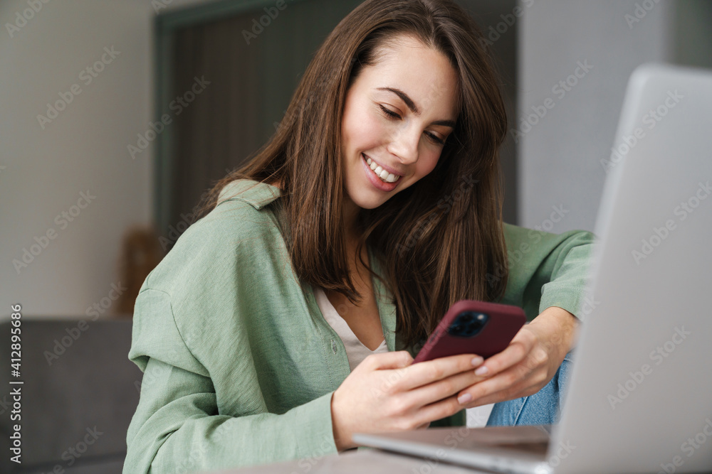 Cheerful beautiful woman using mobile phone while working with laptop Cheerful beautiful woman using mobile phone while working with laptop
