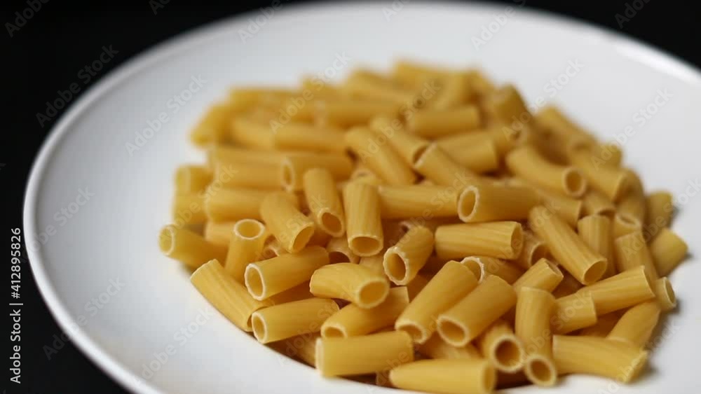 Uncooked rigatoni pasta in the white porcelain plate. Blurry background. Uncooked rigatoni pasta in the white porcelain plate. Blurry background.