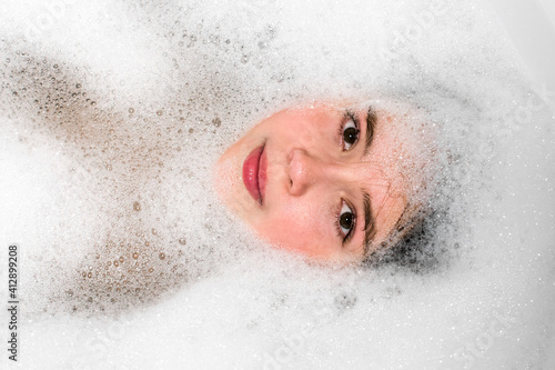 Girl face in  bathtub in water with foam.