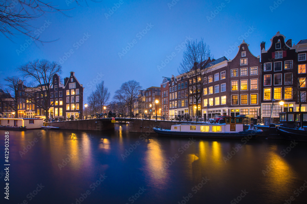 Winter snow night view of Dutch canal and old houses in the historic city of Amsterdam, the Netherlands